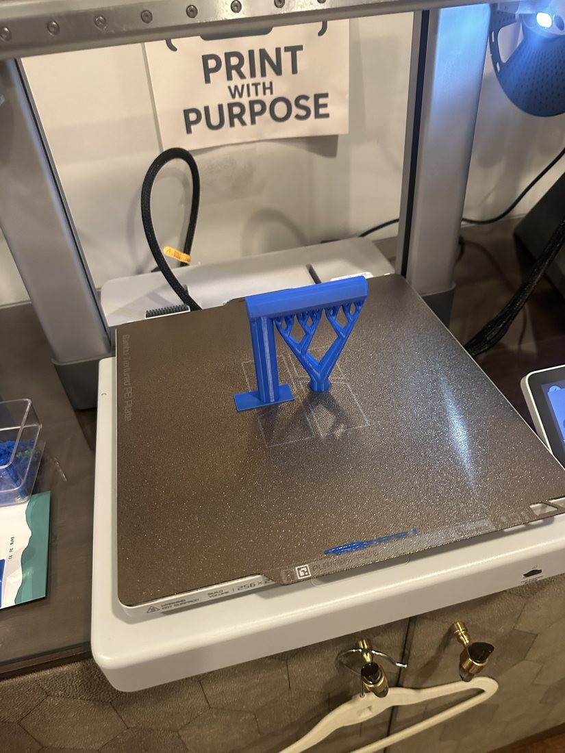 A blue part with tree supports fresh off Jackson's 3D printer, under the Print with Purpose sign